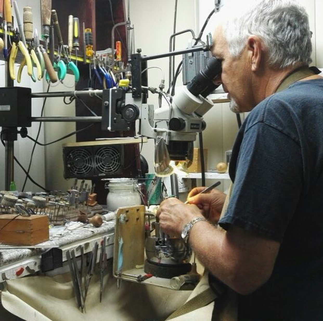 a man, Vernon Wilson, working with jewelry at a workbench using a microscope